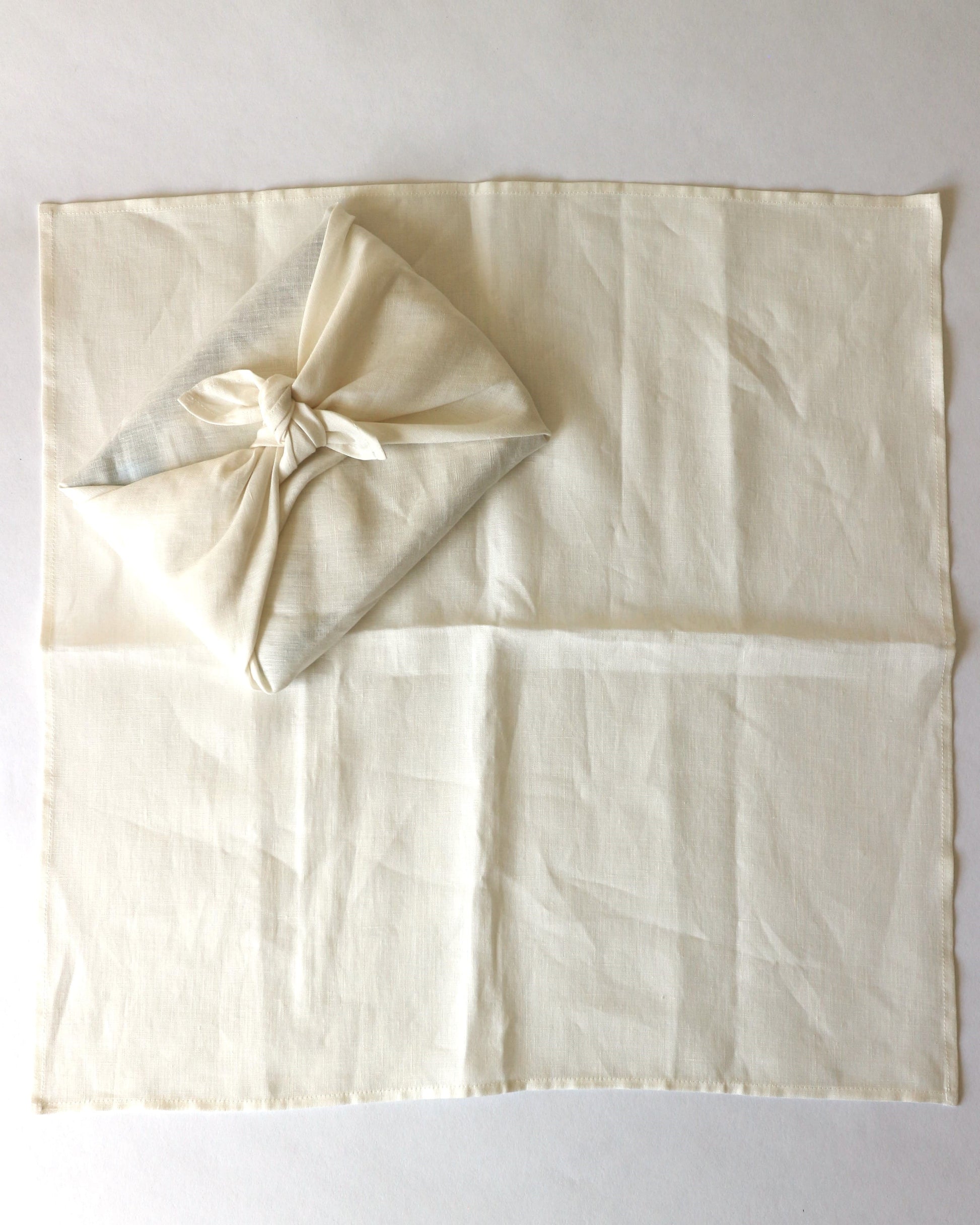 Furoshiki Tuch in weiß aus Bio-Leinen schön verpackt und darunter ein weißes Tuch freigelegt