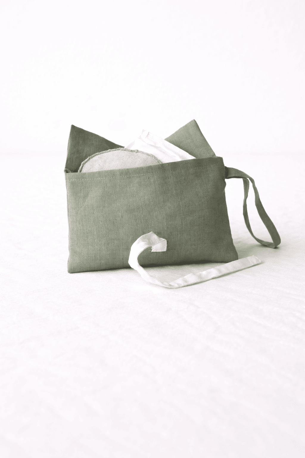 Geöffnete grüne Schminktasche aus Bio-Leinen mit weißen Schleifen